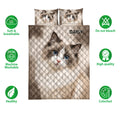 Ragdoll cat quilt bedding display with blue-eyed cat artwork, pillows, and neutral brown tones