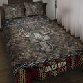 Hunting quilt blanket displayed on a bed with camouflage foliage, antlers, cross artwork, and rustic borders