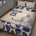 Close bedroom view of a hockey quilt blanket featuring goalie artwork, hockey pucks, and sticks