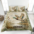 Duck hunting quilt blanket displayed on a bed with mallard artwork, wetland scenery, cattails, and green borders