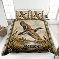 Duck hunting quilt blanket displayed on a bed with mallard artwork, marsh reeds, and rustic plaid borders