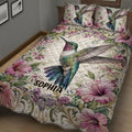 Close bedroom view of a hummingbird quilt blanket with pink flowers and ornate botanical details