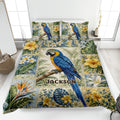 Parrot quilt blanket displayed on a bed with blue macaws, tropical flowers, leafy foliage, and a botanical border