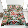 Tropical flamingo quilt blanket spread across a bed with pink flowers, palm leaves, and aqua water scenes