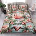 Tropical flamingo quilt blanket styled on a bed with pink hibiscus flowers and lush palm leaves