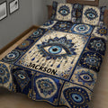 Close bedroom view of an Evil Eye quilt blanket with repeated eyes, floral motifs, and rich navy detail