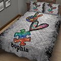 Angled bedroom view of an autism quilt blanket featuring rainbow puzzle pieces, hearts, and awareness artwork