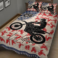 Close bedroom view of a motocross quilt blanket with black dirt bike artwork, red riders, and blue star accents