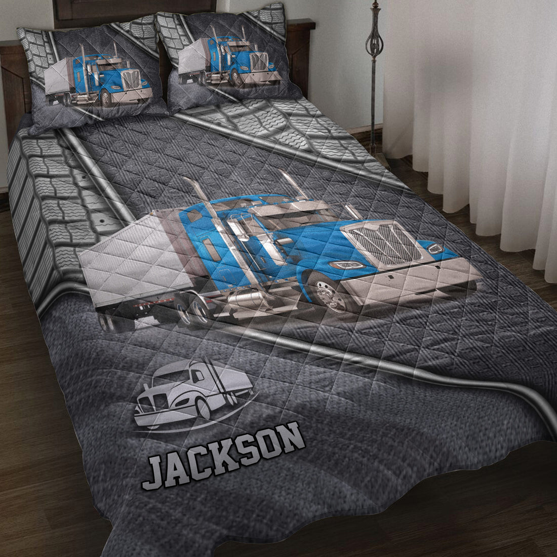 Trucker quilt blanket displayed on a bed with blue semi truck artwork, tire details, and dark gray road-inspired design