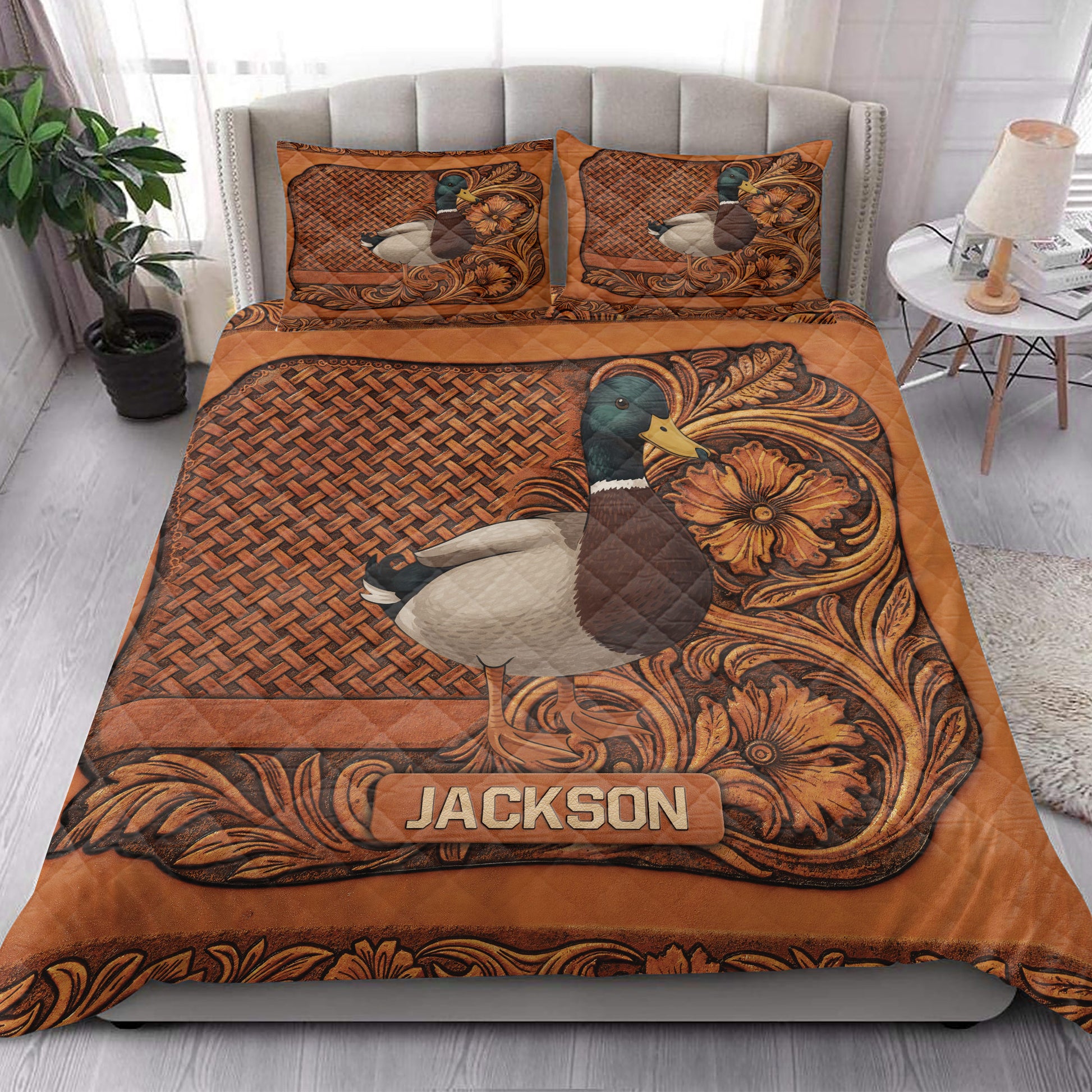 Mallard duck quilt bedding displayed on a bedroom bed with rustic floral borders and copper-brown artwork
