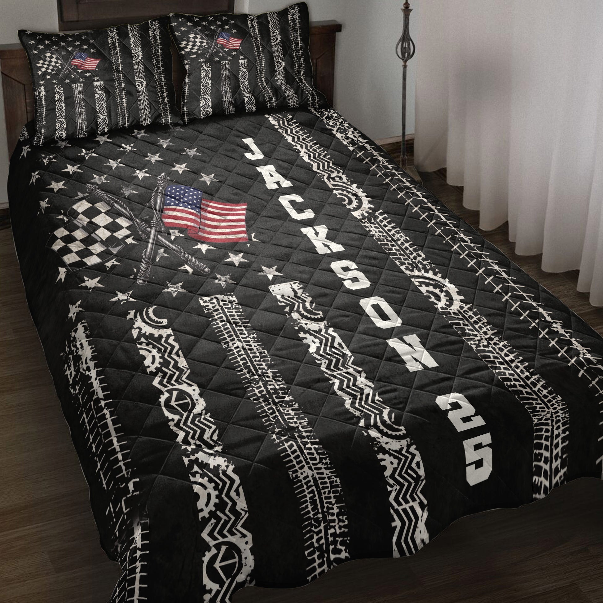 Black racing quilt blanket displayed on a bed with checkered flags, tire tracks, stars, and patriotic artwork