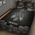 Close bedroom view of a black quilt blanket with large white dreamcatcher and feather artwork