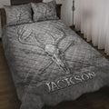 Gray hunting quilt blanket displayed on a bed with deer skull, antler, and crossed arrow artwork