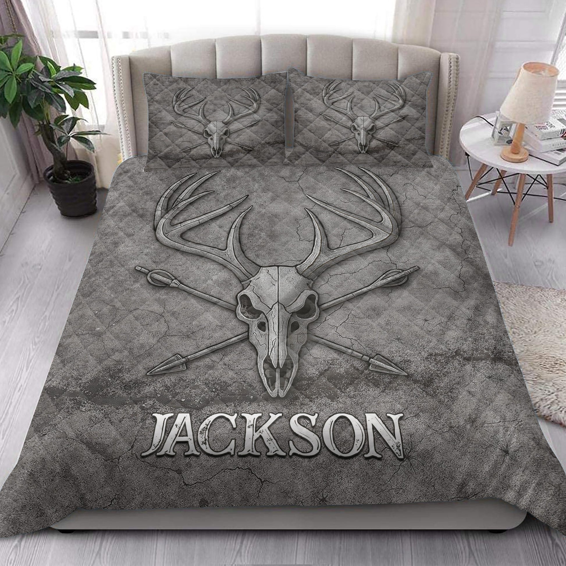 Rustic bedroom styled with a gray hunting quilt blanket featuring deer skull and antler artwork