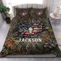 Hunting quilt blanket styled on a bed with large antlers, deer skull artwork, pine branches, and rustic bedroom decor