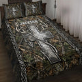 Hunting quilt blanket displayed on a bed with camouflage foliage, deer antlers, arrows, and rustic braided borders