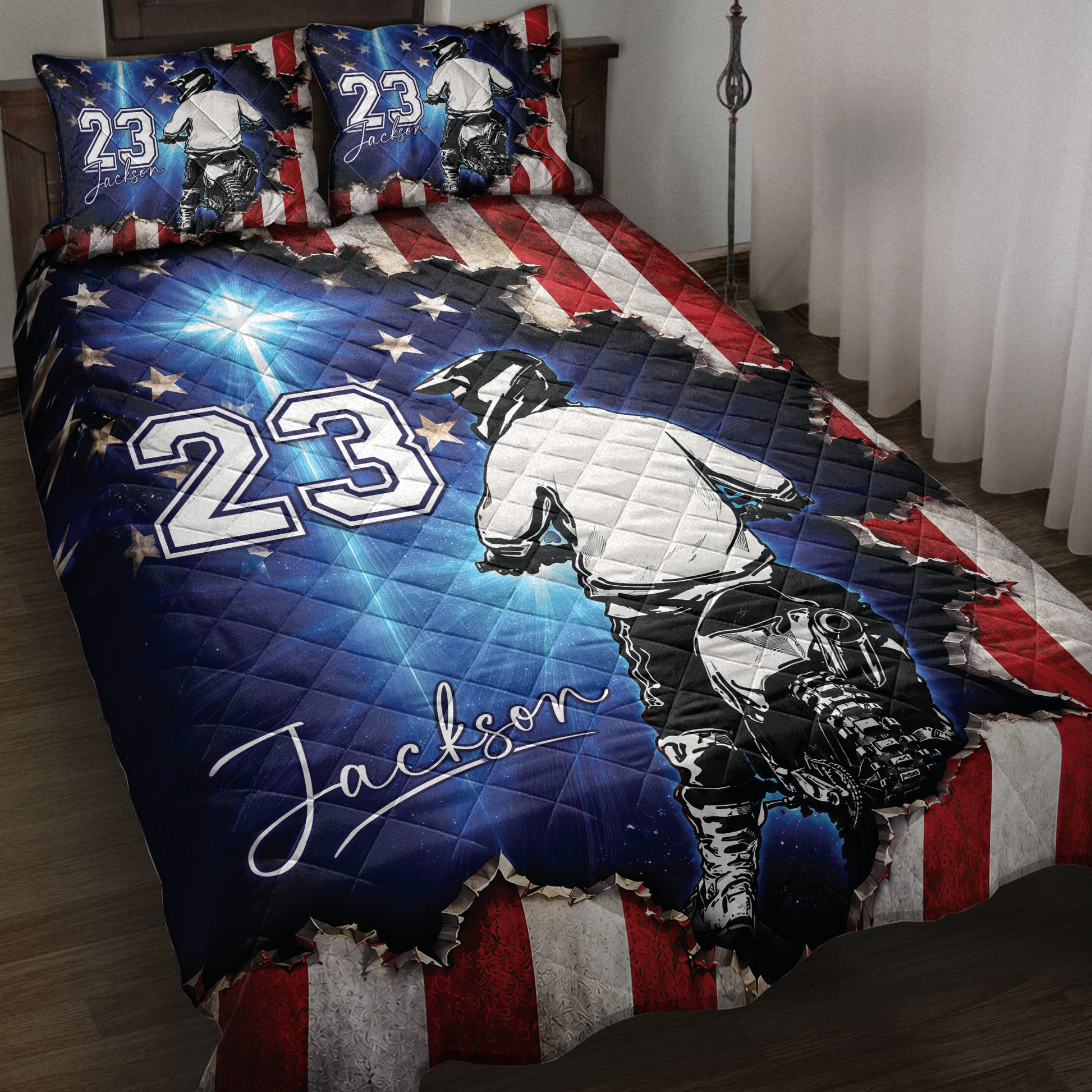 Motocross quilt blanket displayed on a bed with dirt bike rider artwork, stars, and red white blue graphics