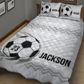 Angled bedroom view of a soccer quilt blanket featuring bold ball artwork and geometric stripes