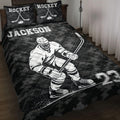 Black hockey quilt blanket displayed on a bed with a hockey player, crossed sticks, puck, skates, and bold sports artwork
