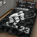 Close bedroom view of a black hockey quilt blanket featuring a helmeted player, stick, skates, puck, and sports graphics