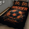 Close bedroom view of a black soccer quilt blanket with bold orange ball graphics
