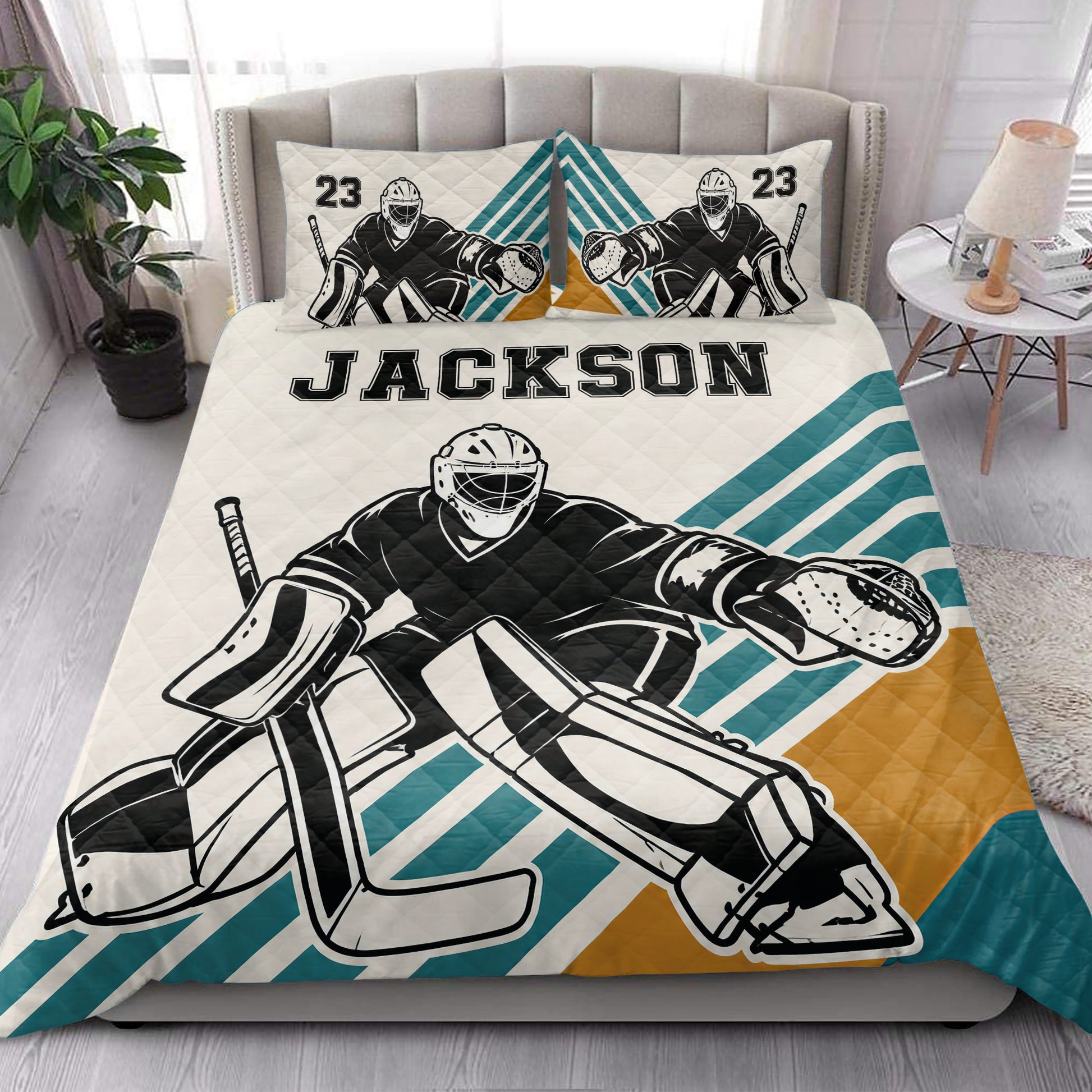 Hockey goalie quilt blanket styled on a bedroom bed with bold teal, white, and gold stripes