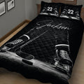 Close bedroom view of a black hockey quilt blanket with skates, sticks, puck and ice details
