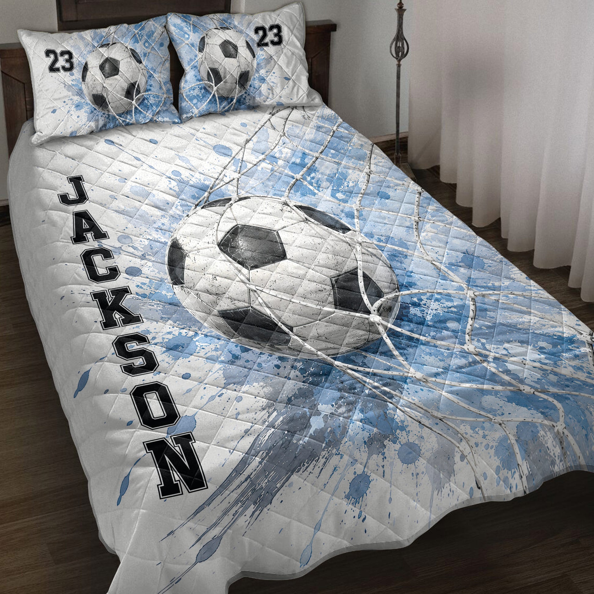 Soccer quilt blanket displayed on a bed with blue splatter artwork, goal net, and soccer ball design