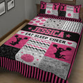 Close bedroom view of a pink and black cheerleading quilt with pom-poms, stars, bows, and megaphones