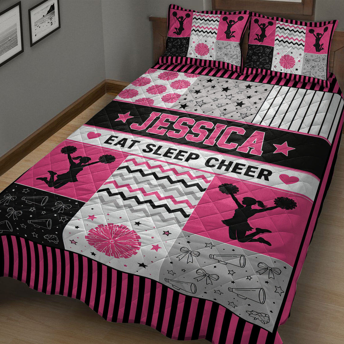 Close bedroom view of a pink and black cheerleading quilt with pom-poms, stars, bows, and megaphones