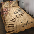 Piano quilt blanket displayed on a bed with musical notes, piano keys, treble clefs, and vintage floral artwork