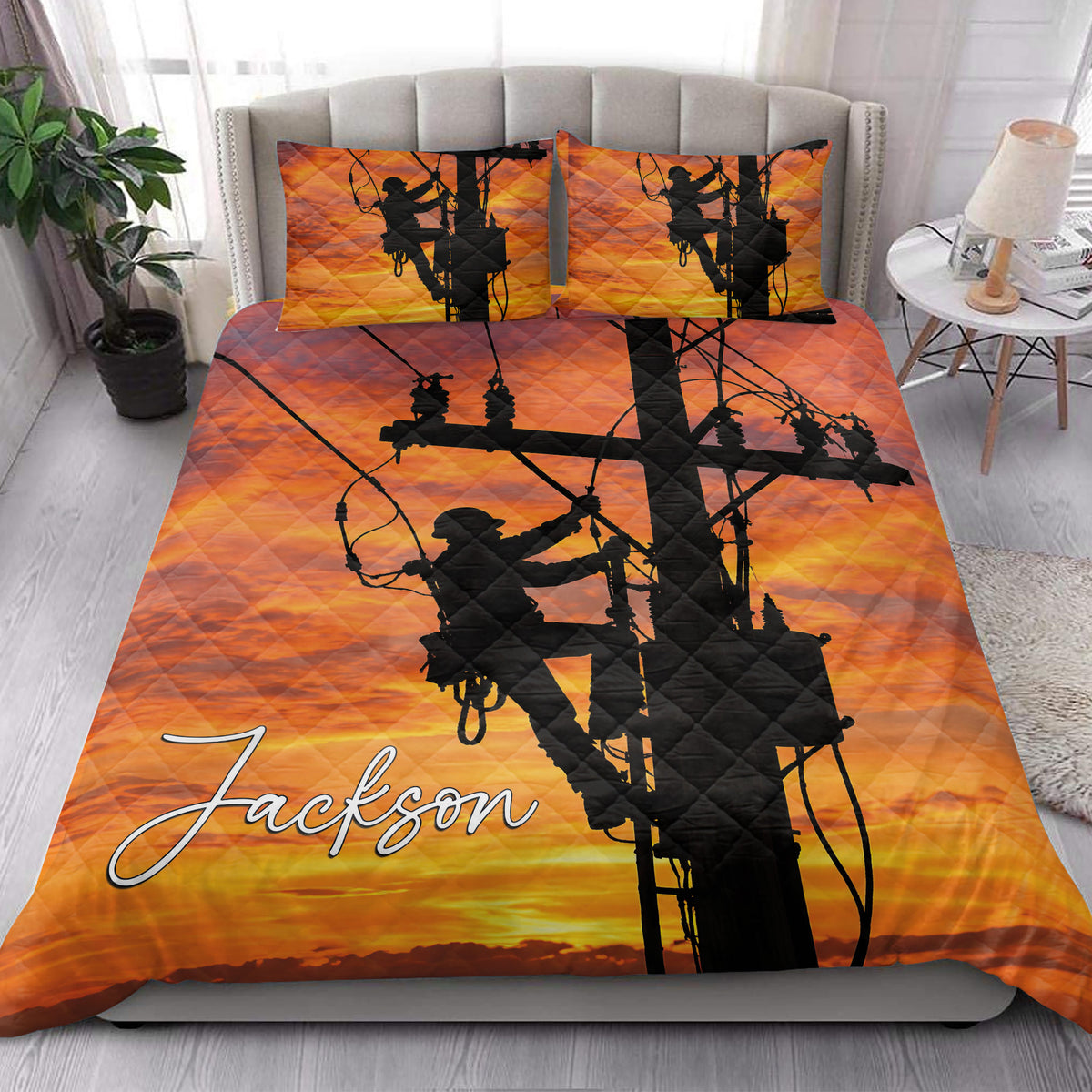 Lineman quilt blanket styled on a bedroom bed with utility worker silhouettes and orange sunset power line artwork
