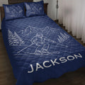 Navy ski quilt blanket displayed on a bed with skier, mountain, and evergreen tree artwork