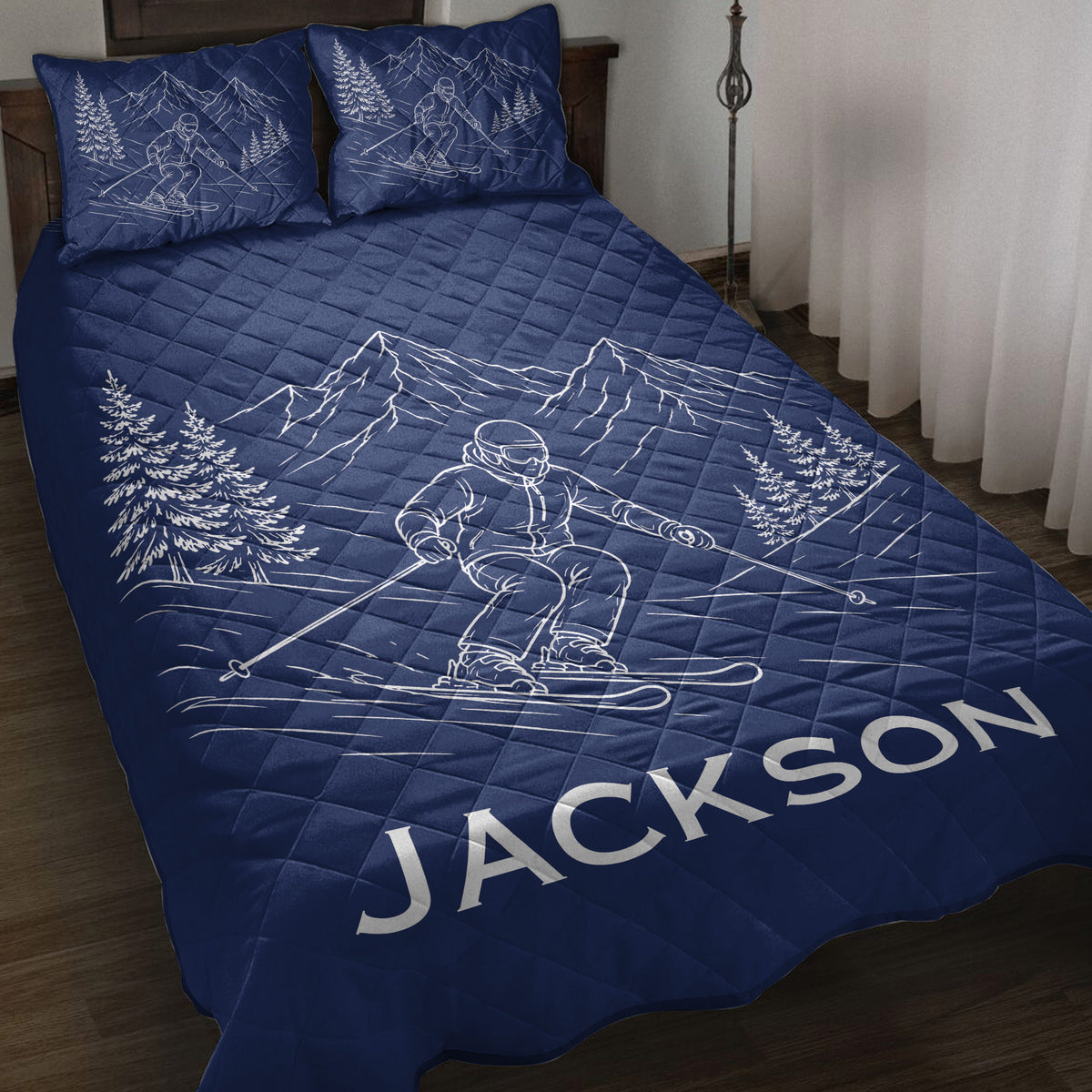 Navy ski quilt blanket displayed on a bed with skier, mountain, and evergreen tree artwork