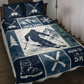 Navy skiing quilt blanket displayed on a bed with mountain artwork, skier imagery, skis, goggles, and snowflakes