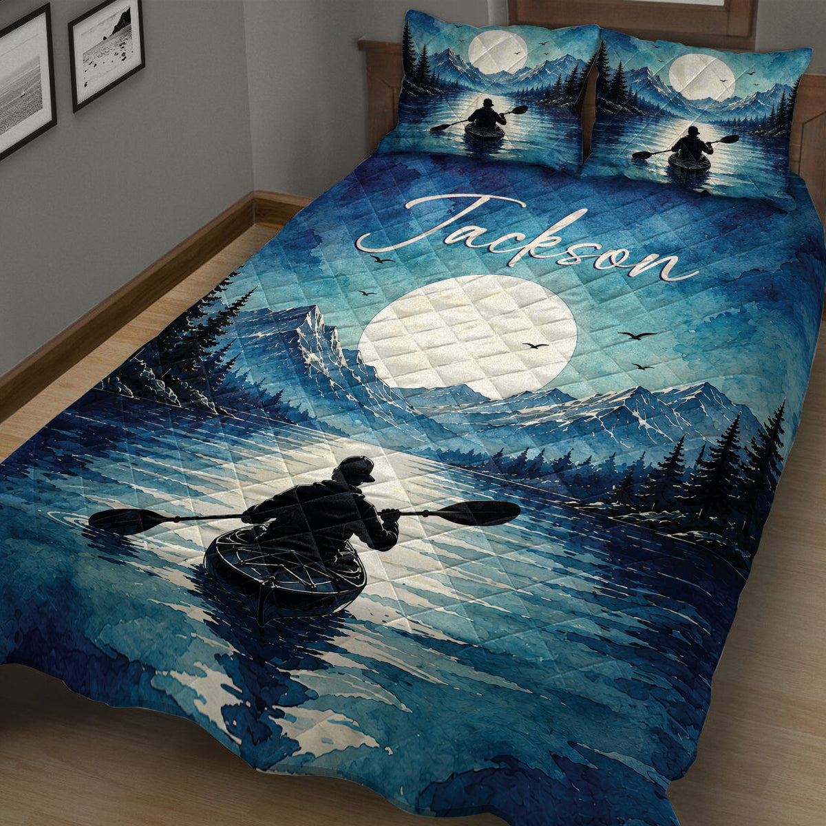 Blue kayak quilt spread across a bed with moonlit mountains, forest scenery, lake water, and paddling artwork