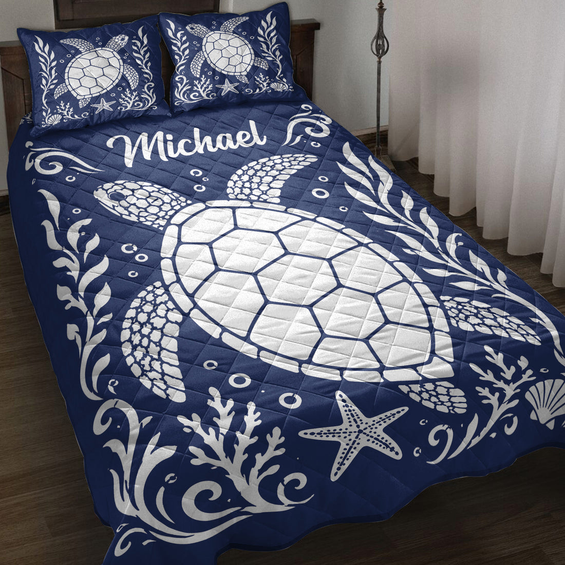Navy turtle quilt blanket displayed on a bed with white sea turtles, coral, shells, and starfish