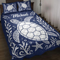 Navy turtle quilt blanket displayed on a bed with white sea turtles, coral, shells, and starfish