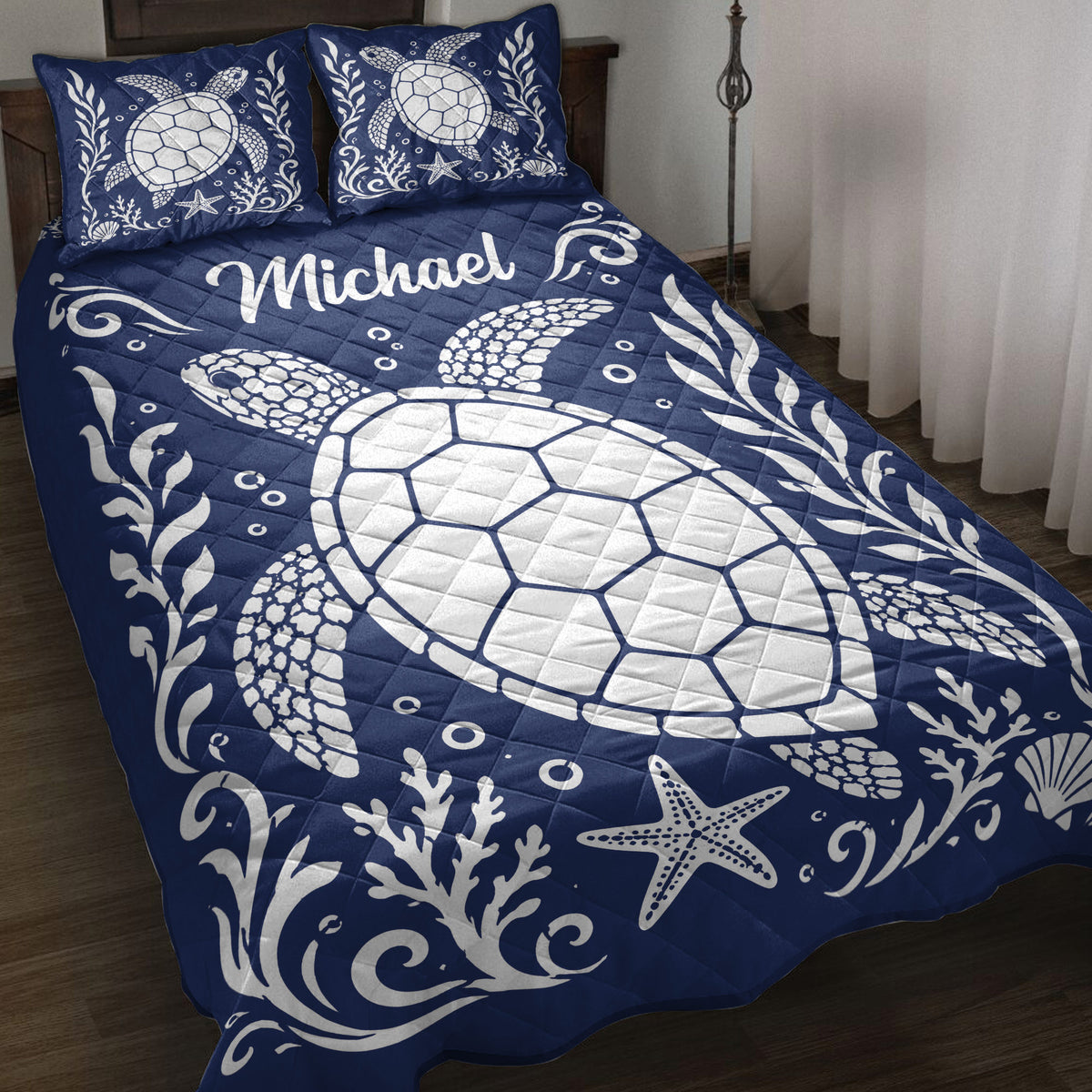 Navy turtle quilt blanket displayed on a bed with white sea turtles, coral, shells, and starfish