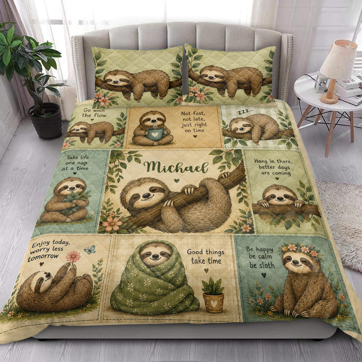 Sloth quilt bedding styled in a bright bedroom with leafy floral artwork and sleepy sloths across the bed