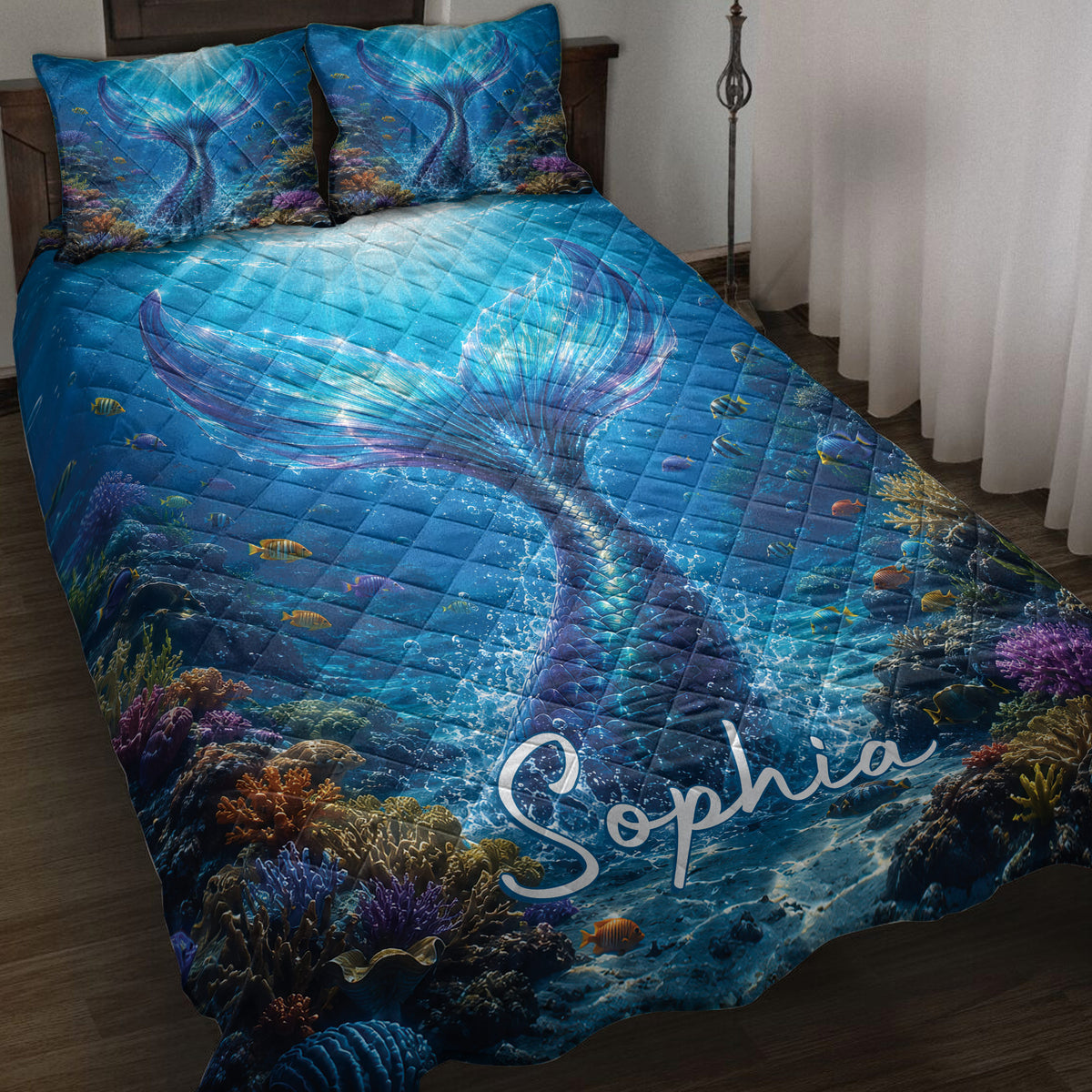 Mermaid quilt blanket displayed on a bed with an underwater coral reef, fish, and vivid blue tail artwork