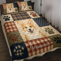 Corgi quilt blanket displayed on a bed with plaid patchwork, paw prints, and warm rustic colors
