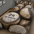 Angled bedroom view of a baseball quilt blanket featuring repeated baseball illustrations and dark accents