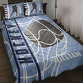 Hockey quilt blanket styled on a bed with blue rink-inspired artwork, hockey sticks, pucks, and player silhouettes