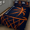 Angled bedroom view of a navy basketball quilt blanket with energetic orange court-inspired artwork