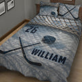 Angled bedroom view of blue hockey quilt blanket featuring sticks, puck, net pattern, and bold sports artwork