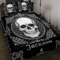 Black skull quilt blanket displayed on a bed with ornate white scrollwork and matching skull pillow designs