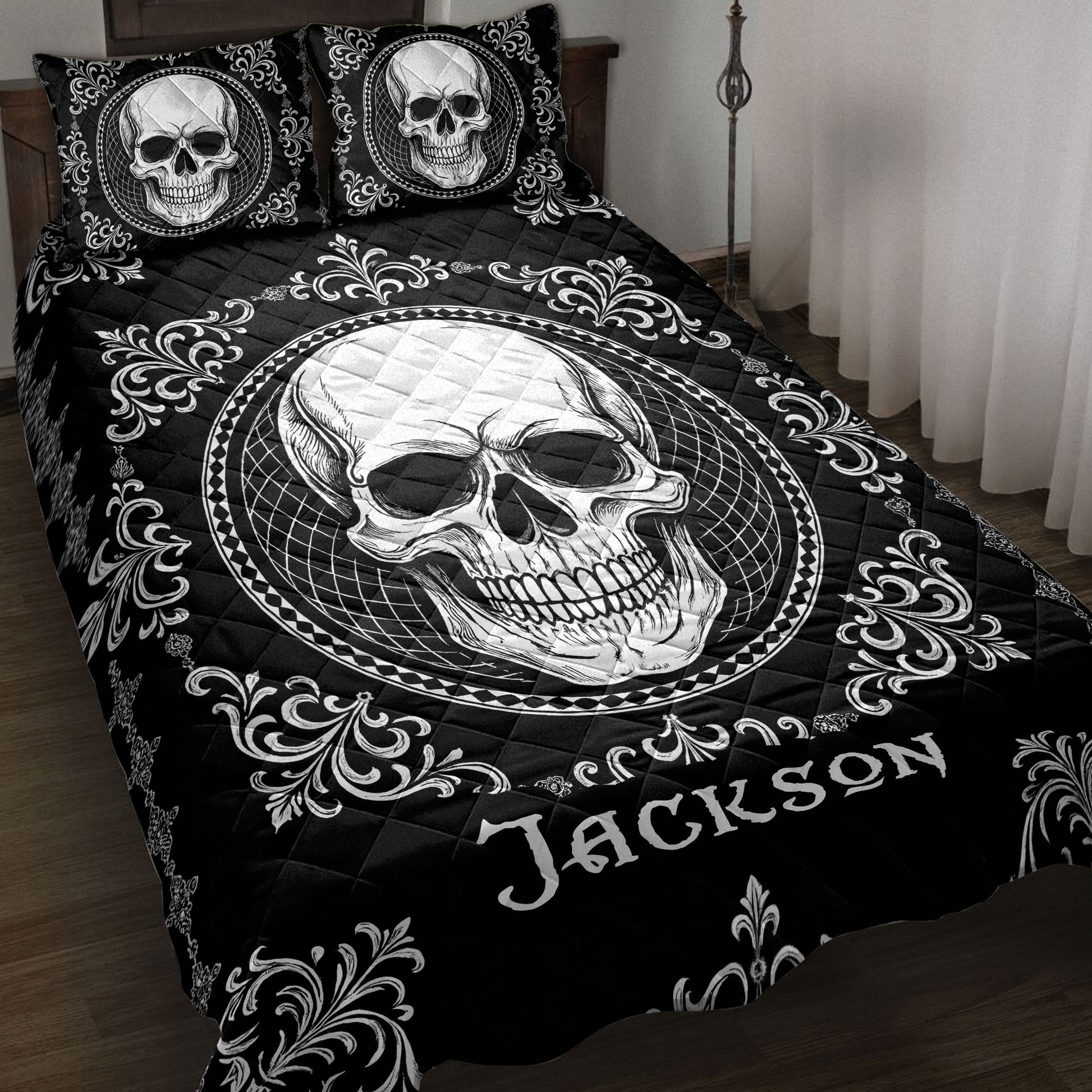 Black skull quilt blanket displayed on a bed with ornate white scrollwork and matching skull pillow designs