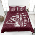 Maroon football quilt blanket shown in a bedroom with player and football design