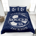 Navy soccer quilt blanket shown on a bed with bold soccer ball graphics and white sports lettering
